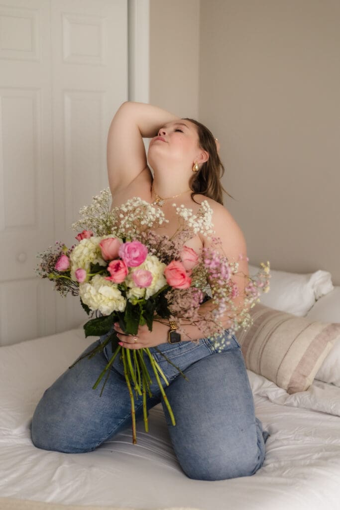 woman with bouquet of flowers poses on the bed during knoxville boudoir photography session