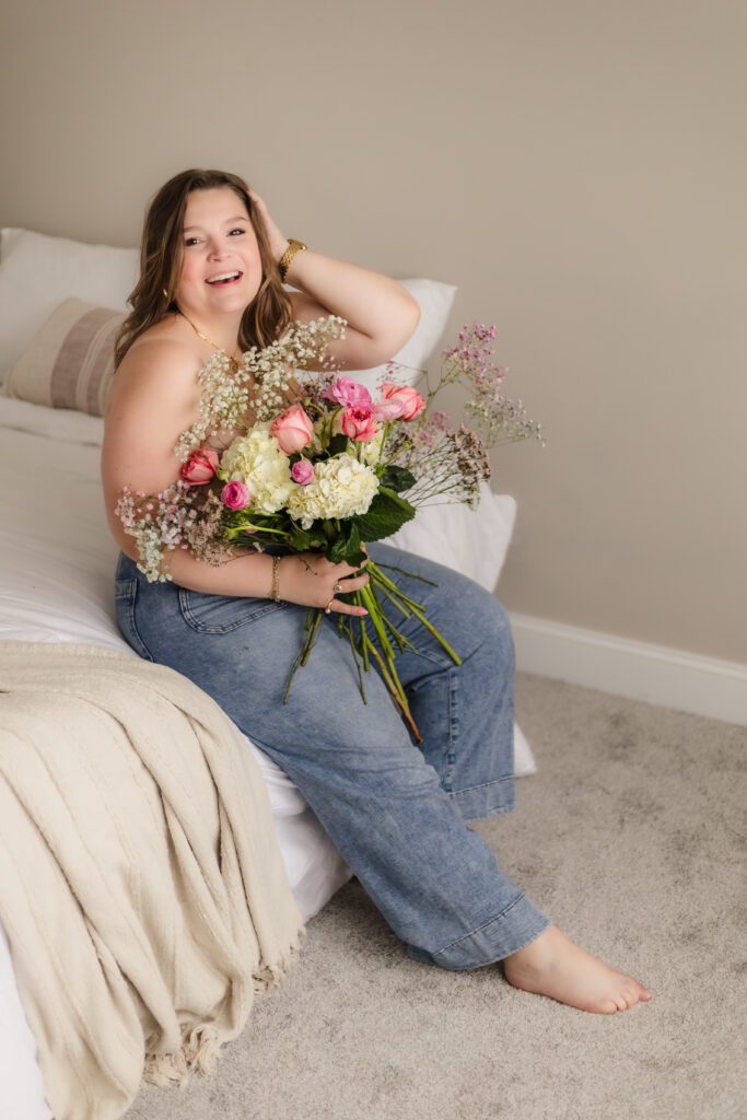 woman sitting on a bed with bouquet of wildflowers during knoxville boudoir photography session