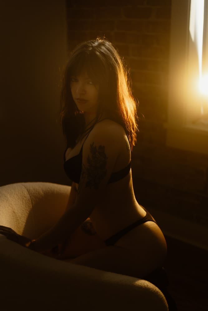woman kneeling on chair looking at camera during golden hour boudoir session at the lightfoot studio in knoxville